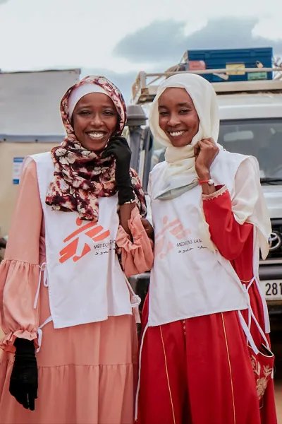 Två kvinnor i msf-västar framför en jeep