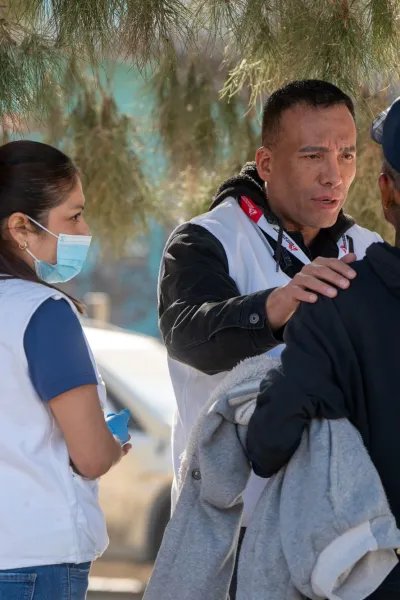 Två personer i vit Läkare Utan Gränser-väst. En av personerna lägger handen på axeln på en tredje person i svart huvtröja.