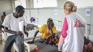 En patient på en sjukhussäng pratar med två läkare