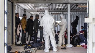 Två personer i skyddsdräkt kontrollerar migranter ombord Ocean Viking