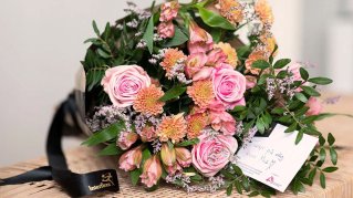 En blombukett med rosa blommor och ett kort med en hälsning på ligger på ett bord