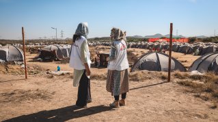 Två kvinnor står och kollar ut över ett flyktingläger.