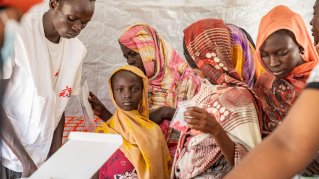 Flicka blickar in i kameran, omgiven av kvinnor och en personal från Läkare Utan Gränser