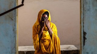 Kvinna i orange klädnad och händerna för ansiktet i en fönsteröppning