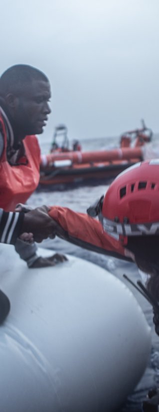 En man får hjälp av Läkare Utan Gränsers medarbetare att ta sig från en vattenfylld gummibåt till vår båt som ingår i vår sök- och räddningsinsats på centrala Medelhavet.