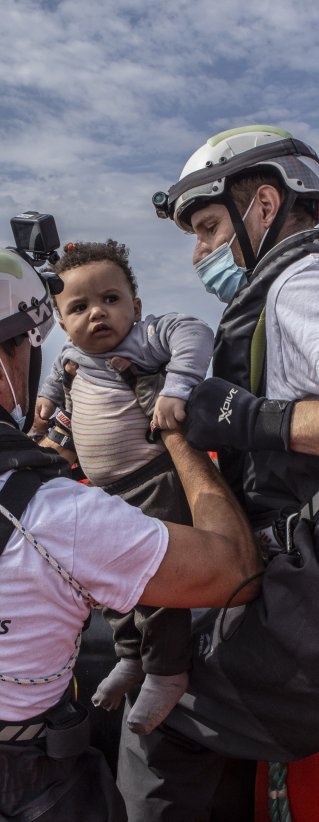 Två medarbetare från Läkare Utan Gränser lyfter upp en liten pojke ur en gummibåt på centrala Medelhavet.