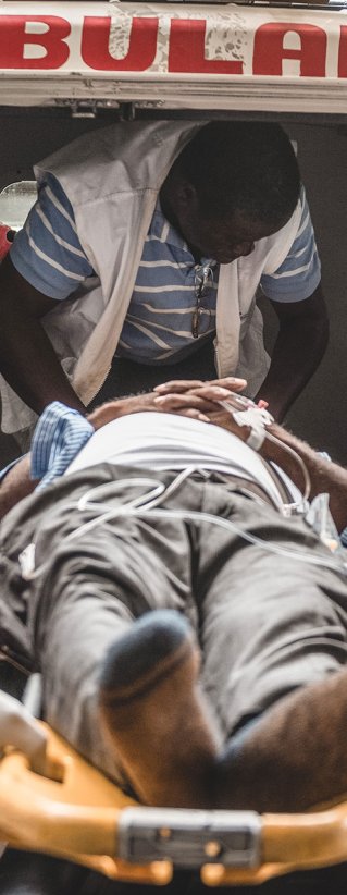 Två sjukhusklädda män bär in en person liggandes på en bår in i en ambulans