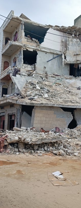 Några personer står framför ett hus som nästan helt har förstörts efter måndagens jordbävning.