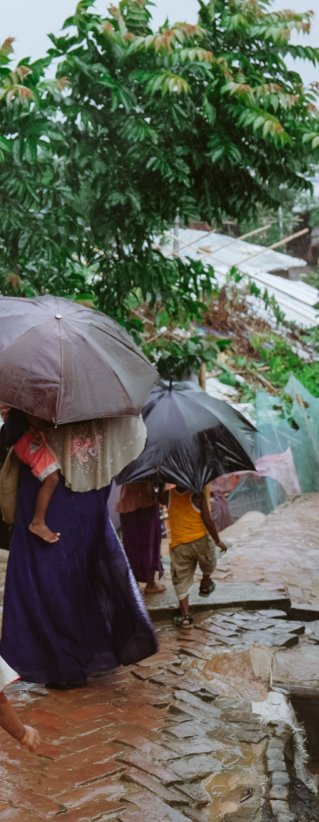 En familj går längs en gata, på båda sidor syns skjul bygda av bambu och plastskivor.