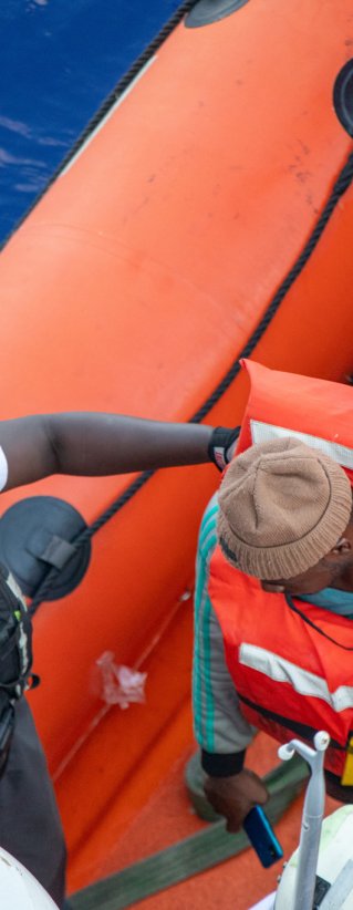 En man iklädd Läkare Utan Gränsers t-shirt hjälper en person av en gummibåt.
