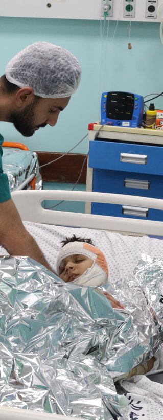 Medicinsk personal vid en sjukhussäng med en pojke med bandage runt huvudet