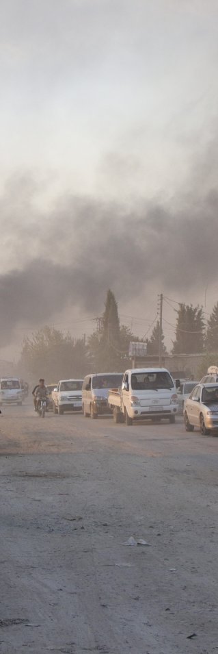 Bilar och människor på en gata framför rök som kommer från bakgrunden