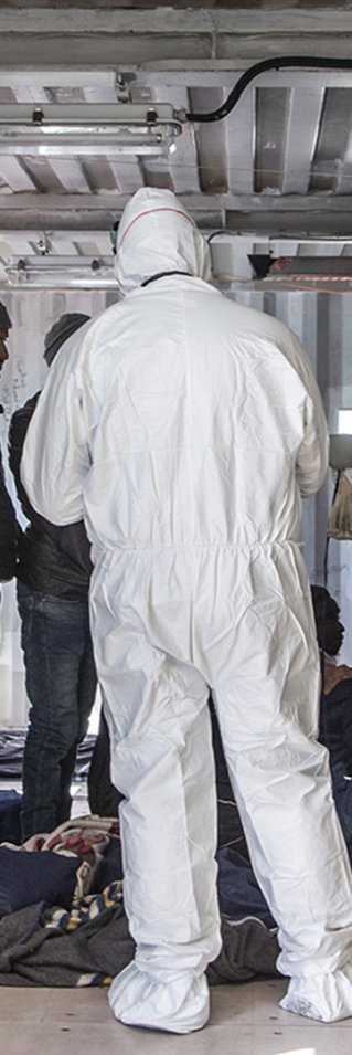 Två personer i skyddsdräkt kontrollerar migranter ombord Ocean Viking