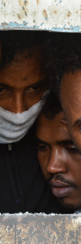 Fyra män tittar ut från ett förvar i Libyen.