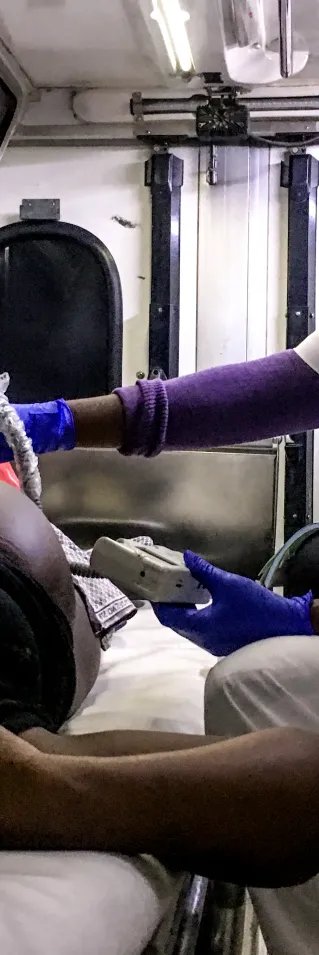 En kvinna gör ett ultraljud på en gravid kvinna som ligger på en bår i en ambulans.