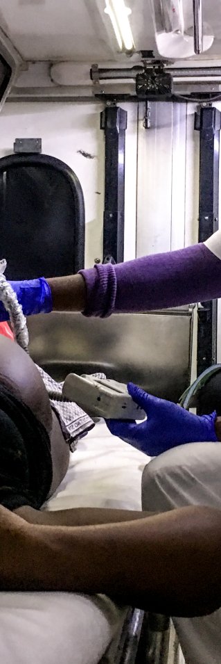 En kvinna gör ett ultraljud på en gravid kvinna som ligger på en bår i en ambulans.