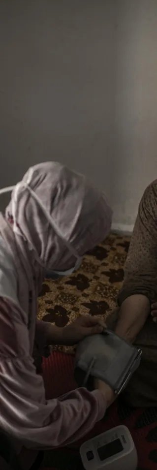 En sjuksköterska mäter blodtrycket på en äldre kvinna som sitter ner.