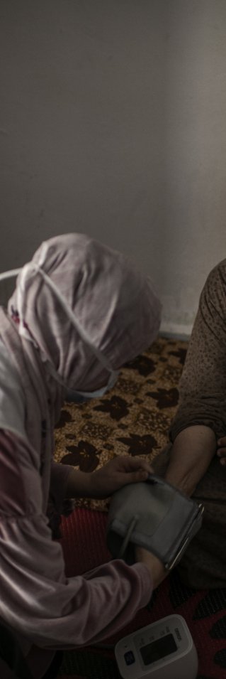 En sjuksköterska mäter blodtrycket på en äldre kvinna som sitter ner.