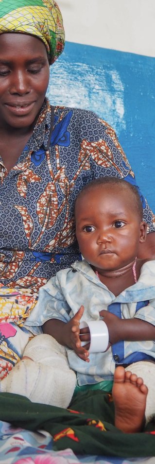 En kvinna sitter på en säng och håller om en liten pojke.