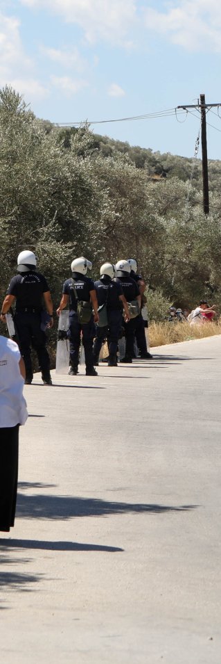 Personal från Läkare Utan Gränser tittar på när polisen för bort demonstranter utanför Moria, på den grekiska ön Lesbos.