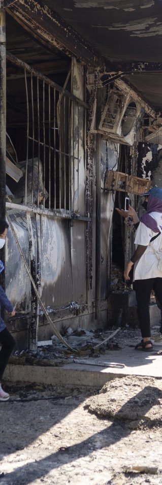 Tre personer står i det som är kvar av Morialägret på den grekiska ön Lesbos.