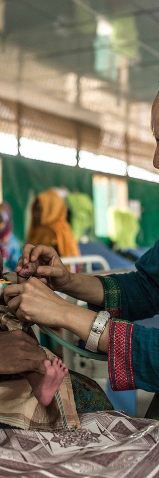 Två kvinnor sitter med sidan mot kamerna, Den ena håller en liten bebis, den andra undersöker bebisen emd stetoskop, iklädd en Läkare Utan Gränser-väst.