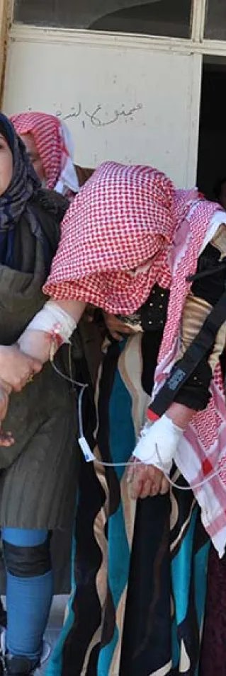 Några kvinnor stöttar en kvinna med dropp utanför en vårdcentral i Abu Qalqal, Syrien.
