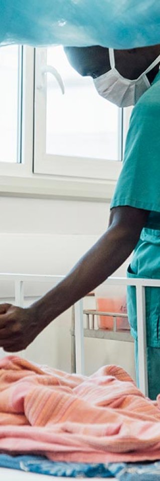 Tvååriga Sheku Kamara, som ligger på sängen på Läkare Utan Gränsers sjukhus i Kenema, Sierra Leone, håller en anställd i handen.