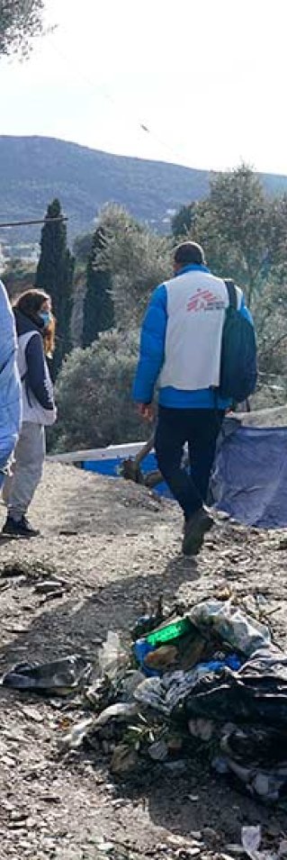 En anställd från Läkare Utan Gränser går, med ryggen mot kameran, på en grusväg genom ett läger på den grekiska ön Samos.