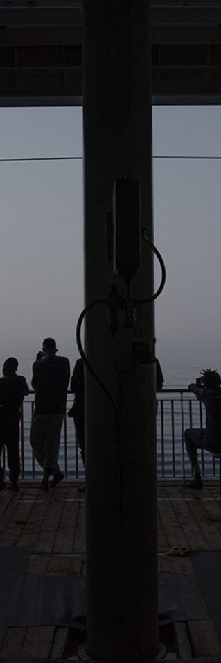 Flera människor står i motljus på däck ombord på sök- och räddningsfartyget Geo Barents och tittar ut mot havet.