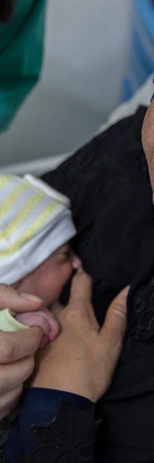 En nybliven mamma på Rafik Hariri sjukhus i Beirut, Libanon, har sitt barn tätt intill bröstet, sjukvårdpersonal står lutad över sängen med en hand på barnet.