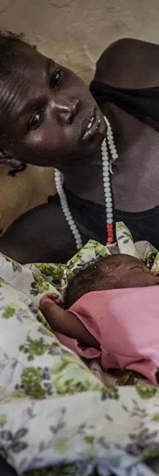 En mamma ligger på en sjukhussäng aå Aweil-sjukhuset i Sydsudan och tittar på sina nyfödda tvillingar som ligger framför henne på sängen.