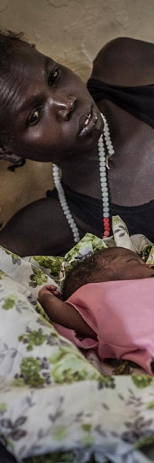 En mamma ligger på en sjukhussäng aå Aweil-sjukhuset i Sydsudan och tittar på sina nyfödda tvillingar som ligger framför henne på sängen.