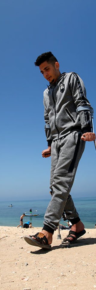 En ung man går på kryckor på en strand i Gaza, Palestina.