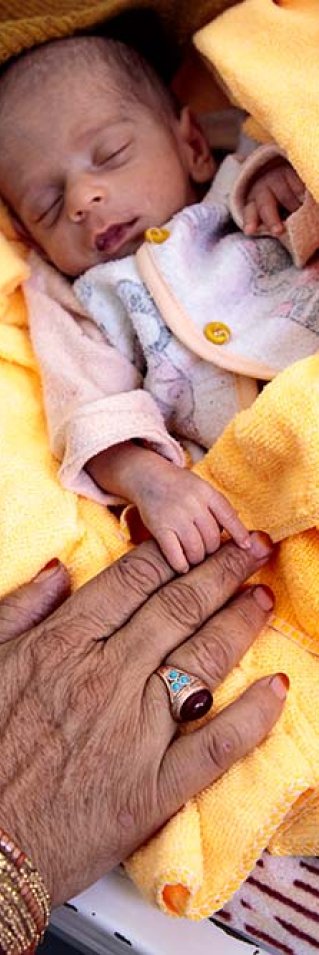 En liten bebis, som är inskriven på Läkare Utan Gränsers undernäringsklinik i Herat, Afghanistan, ligger på en gul filt. En kvinnas händer syns bredvid filten.