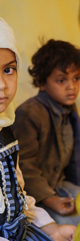 Sjuåriga Asifa sitter på en bänk, bakom henne sitter lillebror Wardan. De bor i ett flyktingläger i Marib, Jemen.