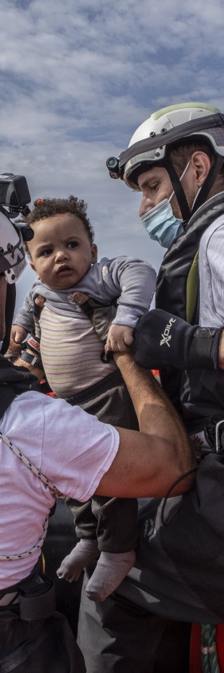 Två medarbetare från Läkare Utan Gränser lyfter upp en liten pojke ur en gummibåt på centrala Medelhavet.