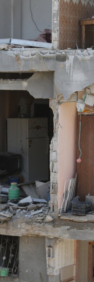 Ett flervåningshus i Gaza, Palestina, som bombats. På en av våningsplanen står en man och tittar ut.