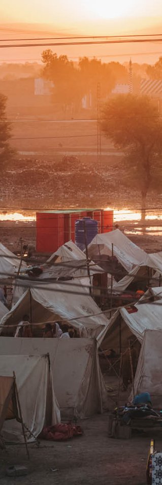 I soluppgången syns ett tältläger med vita tält som står tajt tillsammans. I bakgrunden syns vattnet som har översvämmat stora delar av Pakistan.