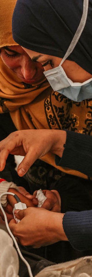 Två kvinnor står vid ett litet barn och kollar på hans hand. 