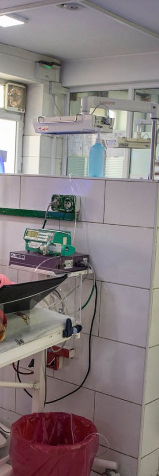 En kvinna står i en sjukhussal bredvid en säng där ett spädbarn ligger.