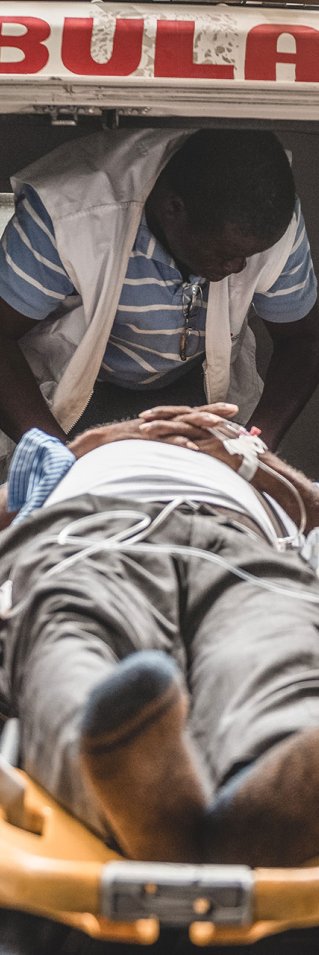 Två sjukhusklädda män bär in en person liggandes på en bår in i en ambulans
