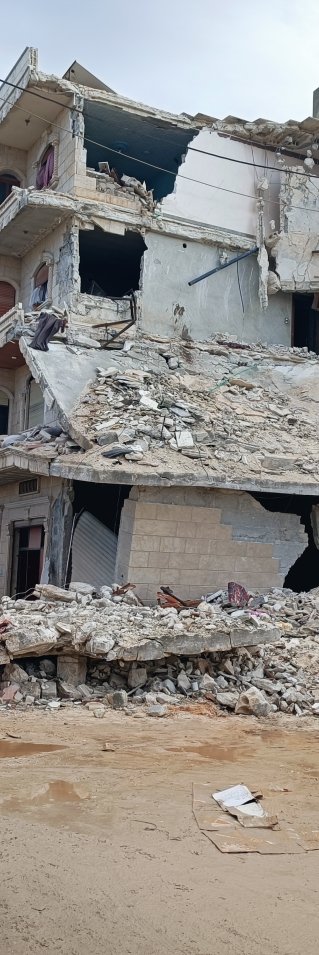 Några personer står framför ett hus som nästan helt har förstörts efter måndagens jordbävning.