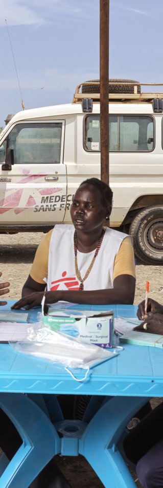 Tre personer i Läkare Utan Gränser västar sitter runt ett bord och diskuterar.