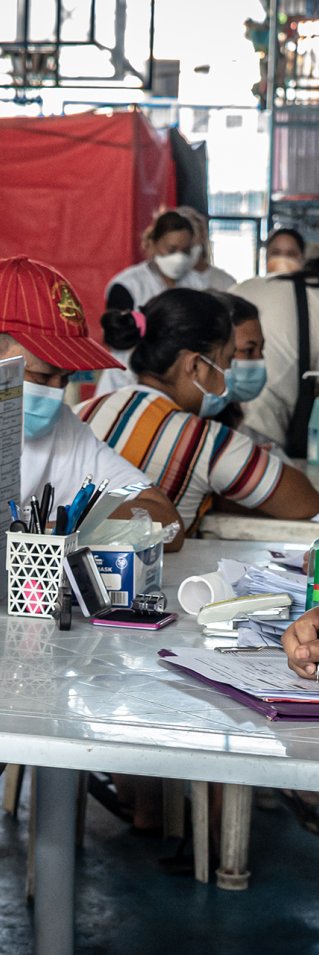 En kvinna i Läkare Utan Gränsers t-shirt sitter vid ett bord. Mittemot sitter en ung kille med munskydd.