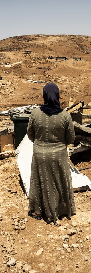 Framför några ruiner står en kvinna med ryggen mot kameran.