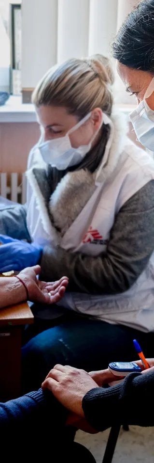 Två kvinnor tar blodprov och kollar pulsen på en äldre kvinna.