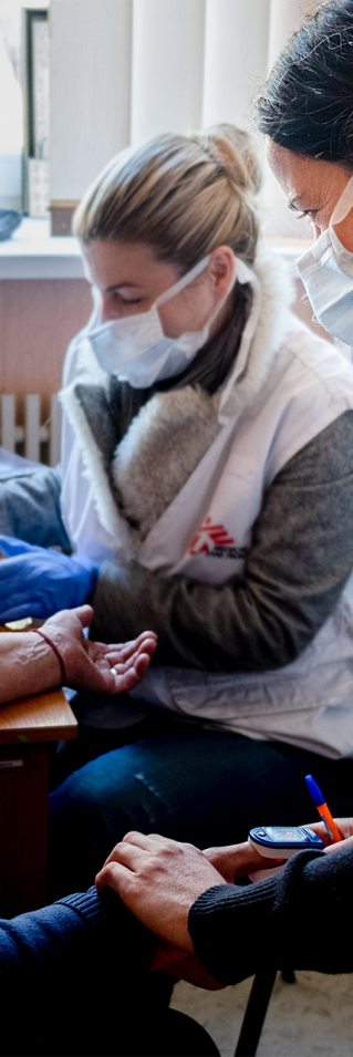 Två kvinnor tar blodprov och kollar pulsen på en äldre kvinna.