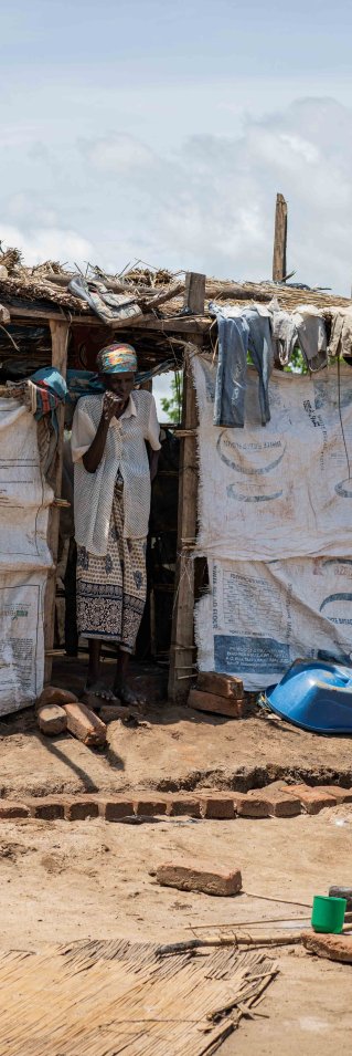 En kvinna lagar mat över öppen eld framför ett skjul byggt av plankor och plastskynken.
