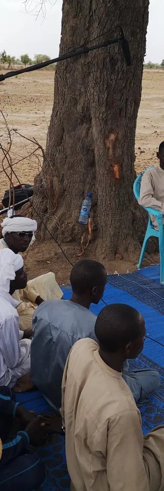 En grupp män sitter i en cirkel. En kvinna hållandes en mikrofon står bredvid.